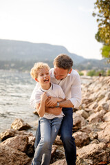 Brunette father and his blondie curly hair son having fun and tickle at the stones of Italian Garda lake 