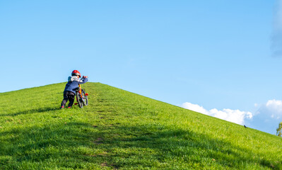 A little boy is trying to climb the hill on his bike. Child development, cycling and children cycling. educational and development activities. Activities in nature. Perseverance and determination.