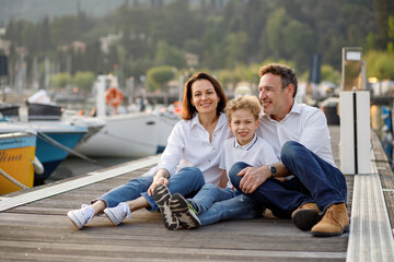 Cute stylish family having fun and smiling on the wooden pier at Italian Garda lake on vacations