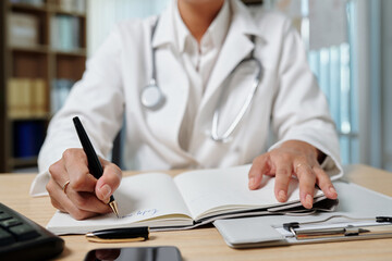 Fototapeta premium Cropped image of general practitioner filling planner when working at desk in medical office