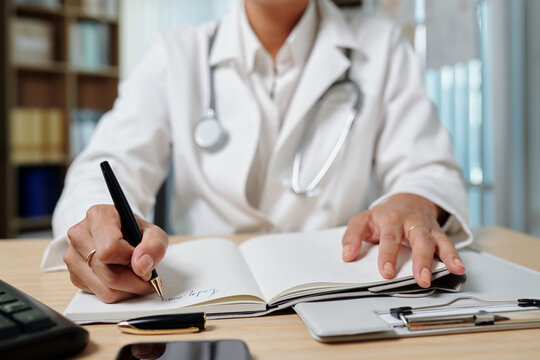 Cropped image of general practitioner filling planner when working at desk in medical office