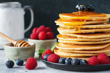 Delicious pancakes, with fresh blueberries, raspberry and maple syrup or honey on a dark background