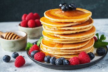 Delicious pancakes, with fresh blueberries, raspberry and maple syrup or honey on a dark background