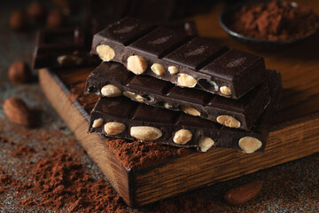 Dark and milk chocolate with nuts on a dark background sprinkled with cocoa powder.