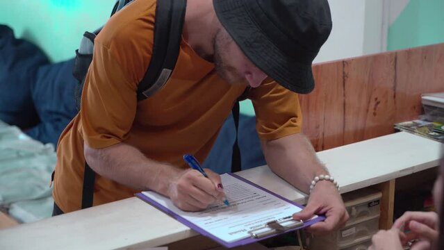 Caucasian man traveling alone register or check in at hostel, receptionist giving information sitting at counter welcoming new customer. lifestyle backpacker traveling low cost expenses concept.

