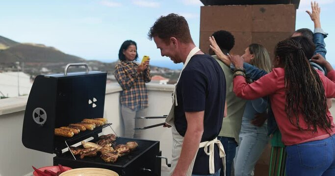 Multi generational people doing barbecue during weekend day at home's rooftop - Multiracial friends having fun smiling on camera while asian woman taking a picture with mobile phone