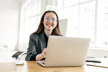 A woman smiles at a creative person in formal clothes on the Internet, using a laptop. Good education and training online on the school's website and app.