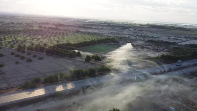 Aerial drone backward moving shot over RCD road in Baluchistan surrounded by agricultural farmlands during morning time. White fog.