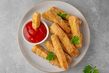 Baked crispy garlic parmesan zucchini sticks served with tomatoes sauce on a gray concrete background. Vegetarian healthy dish. Selective focus.