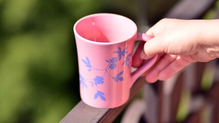 Hand holding coffee mug while standing on balcony.