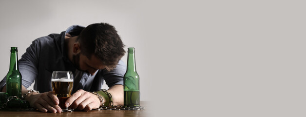 Suffering from hangover. Man chained with glass of alcoholic drink at table against white...
