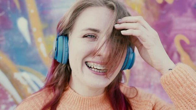 Portrait of a young laughing girl with braces listening to music in headphones in the summer on the street