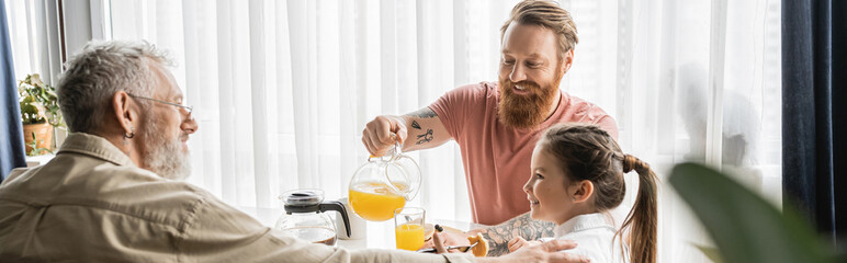 Smiling gay man pouring orange juice near daughter and partner at home, banner. 