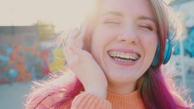 Portrait of a young laughing girl with braces listening to music in headphones in the summer on the street
