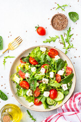 Spring salad in craft plate. Spinach, arugula, tomatoes and feta with olive oil. Top view, vertical on white.
