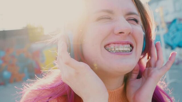 Portrait of a young laughing girl with braces listening to music in headphones in the summer on the street