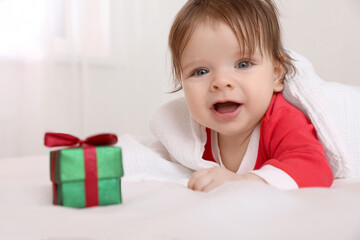 Fototapeta na wymiar Cute baby wearing festive Christmas costume with gift box in crib, closeup