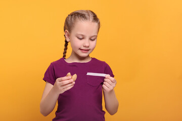 Cute girl holding tasty fortune cookie and reading prediction on orange background