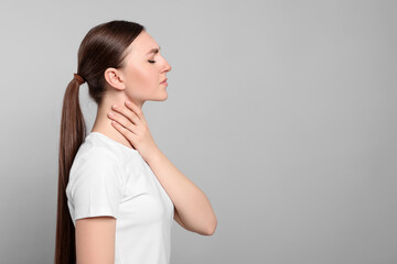 Young woman with sore throat on light grey background. Space for text