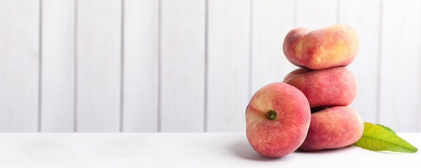 Stack of fresh flat peaches on white table. Banner design with space for text