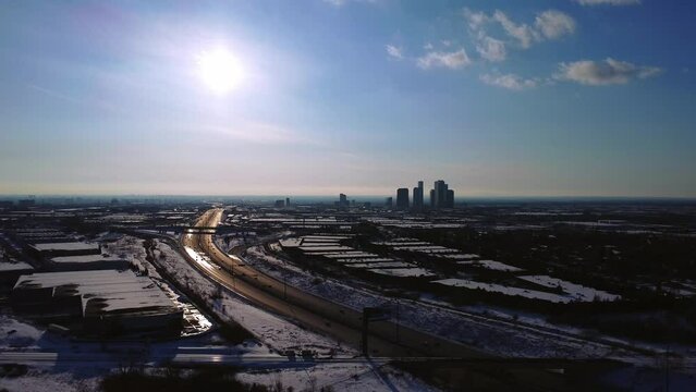 Sunny aerial view of 407 ETR highway with car traffic during winter in Vaughan Ontario with snowy industrial units and highrise condos in distance