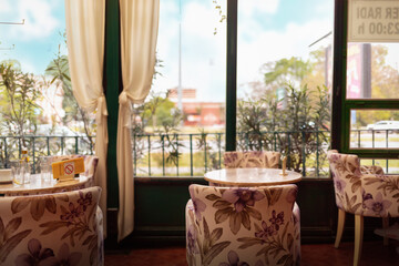 Vintage coffee shop interior with beautiful armchairs, wooden furniture and big windows. View of park