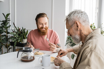 Fototapeta na wymiar Tattooed homosexual man looking at partner during breakfast at home. 
