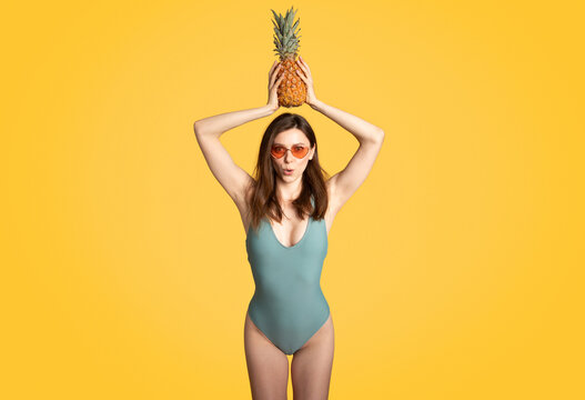 Portrait of playful young woman holding pineapple on head, having fun and posing isolated on vivid yellow background Generative AI