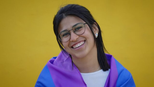 Young smiling lesbian rainbow flag on shoulders isolated yellow background. Happy homosexual and bisexual people pose cheerful looking at camera for studio photo. LGBT pride concept.