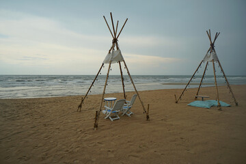 A wooden teepee style with a set of tables and chairs on the beach.