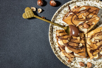 Homemade thin crepes with chocolate spread, banana and hazelnuts. breakfast or dessert. banner, menu, recipe place for text, top view - obrazy, fototapety, plakaty