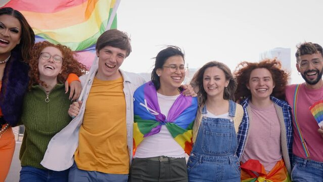 Group of young cheerful friends strolling together on day of gay pride parade in city. People LGBT community pose hugging looking smiling at camera outdoor. Generation z and sexual