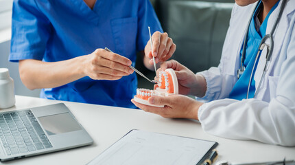 Dentist sitting at table with jaw samples tooth model and working with tablet and laptop in dental office professional dental clinic. medical doctor working.