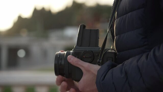 Close up of medium format film photo camera in male hands with bokeh at background