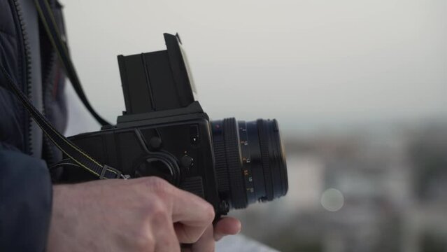 Close up of medium format film photo camera in male hands with bokeh at background