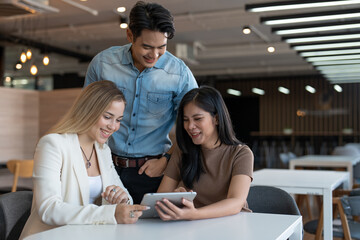 Diverse group of young women and man enjoying and looking in tablet computer on table at modern workplace. Businesspeople working on social media strategy using a digital tablet.