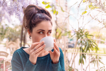 Portrait of pretty young caucasian woman drink cup of coffee in vintage cafe with blooming wisteria. Relaxation and happiness