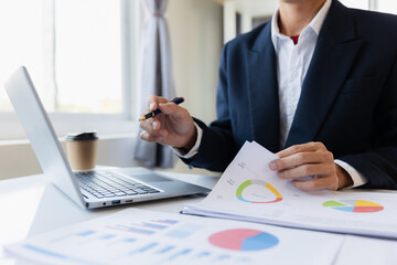 Asian businessman working at office with laptop, tablet and graph data sheet on his desk.