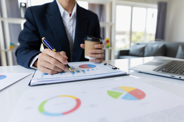 A business man working on a laptop comparing details from graphs Business income chart in real estate, tax, management, marketing, technology in private office.