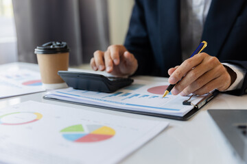 A business man working on a laptop comparing details from graphs Business income chart in real estate, tax, management, marketing, technology in private office.