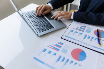 A business man working on a laptop comparing details from graphs Business income chart in real estate, tax, management, marketing, technology in private office.