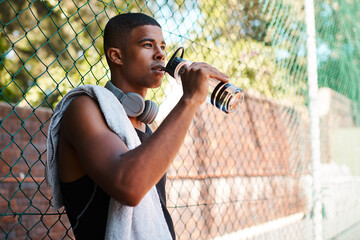 Taking a breather to get some energy. a sporty young man drinking water while standing against a...