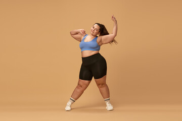 Fototapeta na wymiar Young overweight woman training in sportswear against brown studio background. Losing weight with fitness and diet. Concept of sport, body-positivity, weight loss, body and health care