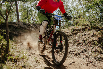male racer cyclist riding dusty trail downhill race in forest, summer mountainbike championship