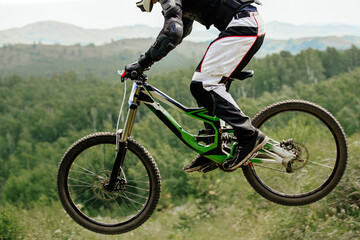 athlete cyclist downhill jumping on background forest and mountains, summer mountainbike...
