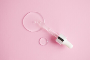 Glass pipette and drop of facial serum or oil on light pink background. Drop of liquid gel with...