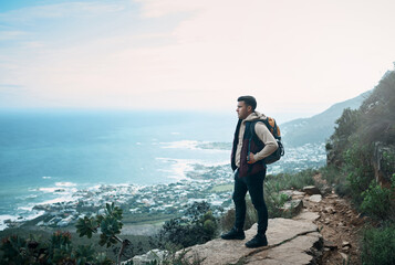 The sound of nature is the best there is. a young man looking at the view from a cliff while out on a hike.