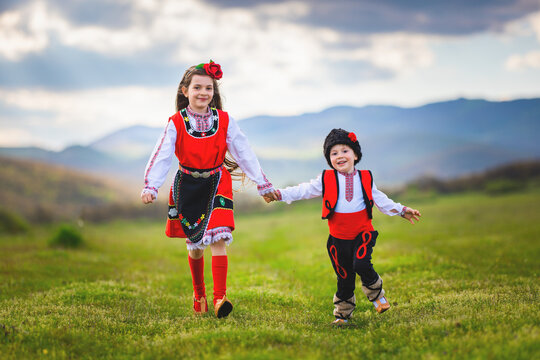 Freedom bulgarian girl and boy with traditional ethnic folklore costumes running on a green lawn in the countryside in Bulgaria