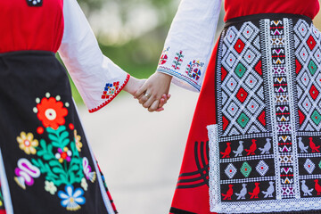 Girls in traditional bulgarian ethnic costumes with folklore embroidery holding hands. The spirit of Bulgaria - culture, history and traditions. - obrazy, fototapety, plakaty