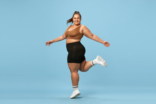 Young, Happy, Active, Overweight Woman Training In Sportswear Against Blue Studio Background. Self-love And Acceptance. Concept Of Sport, Body-positivity, Weight Loss, Body And Health Care